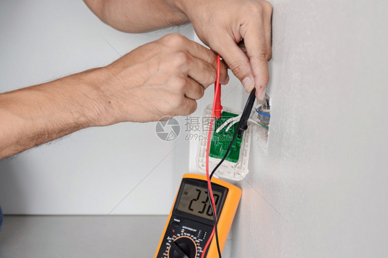 数字的手技术员电工正在用一个数字仪测量墙上电源出口的压以测量墙上的电压图片