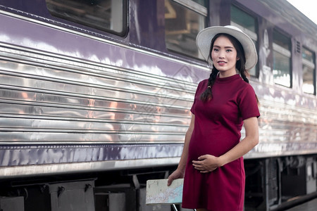 白种人手在火车站旅行时身着红裙子的亚洲孕妇持有一张带红色行李箱的在火车站旅行时身穿红色衣服的亚洲妇女在夏季假期概念泰国旅行者携带图片