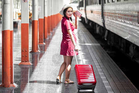 人们白种手提箱在火车站旅行时身着红裙子的亚洲孕妇持有一张带红色行李箱的在火车站旅行时身穿红色衣服的亚洲妇女在夏季假期概念泰国旅行图片