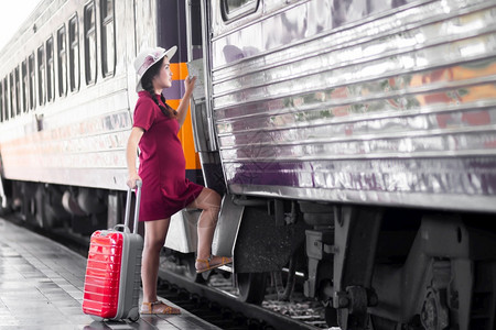 乘客生活在火车站旅行时身着红裙子的亚洲孕妇持有一张带红色行李箱的在火车站旅行时身穿红色衣服的亚洲妇女在夏季假期概念泰国旅行者携带图片