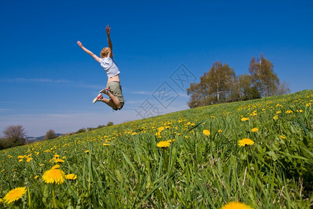 年轻女子在花朵茂盛的草原上玩得开心随意的美丽跳图片