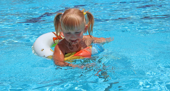 孩子在蓝水中放松橡皮圈游泳池里微笑的女婴和在游泳池里的有花粉女婴在充气圈上游泳的池里来去的Plaitssweakingcreas图片