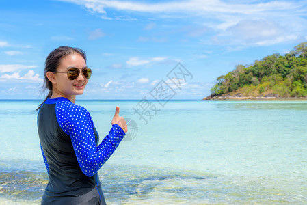 樽尾身穿蓝泳装和太阳镜的快乐女穿着蓝泳装和太阳眼镜带着拇指在海边滩蓝色天空下的岛屿上笑脸夏天背景在泰国高利普附近的拉维泰国欢乐女图片