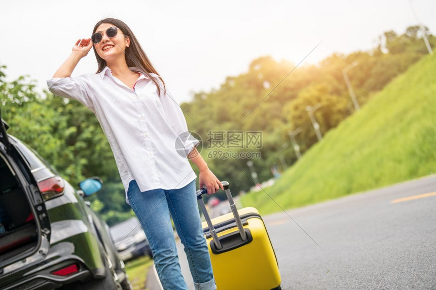 有太阳眼镜的亚洲美容妇女独自在公路旅行时拖着黄色手提行李人们的生活方式和假期概念自然与夏季背景乘坐汽车冒险的女孩有行走之旅大自然图片