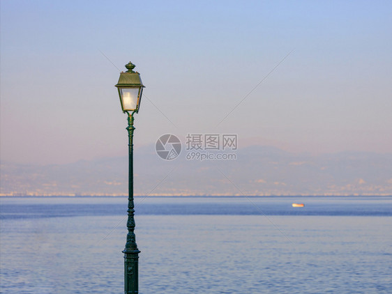 城市的在海湾风景背下由日落的光照亮了一条街灯夜晚阳光和日落太照亮了一条街灯电泡黑色的图片