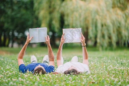 人们背部女孩男朋友和在公园里放松看户外的书躺在公园里的浪漫情侣在公园里看书图片