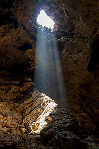 太阳光照耀在自然界的石地板上在泰国的洞穴中游客黑暗海图片