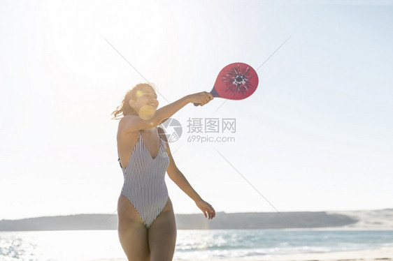男人追求微笑的年轻女子海滩打网球闲暇图片