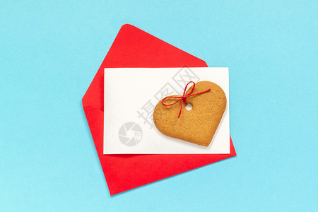迷人的红信封有空白纸牌用于文字和心形姜饼干紧贴在蓝背景上翻版空间以爱打字问候与红色信封白纸卡用于文字和心形姜饼干蓝背景上烘烤的天图片