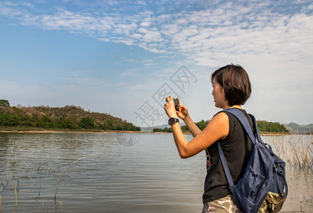 山一位年轻女使用智能手机的侧面观点并用它来拍摄湖边海岸的照片其背景包括技术节假日旅行生活方式自然没有重点具体来说就是无足轻重美丽图片