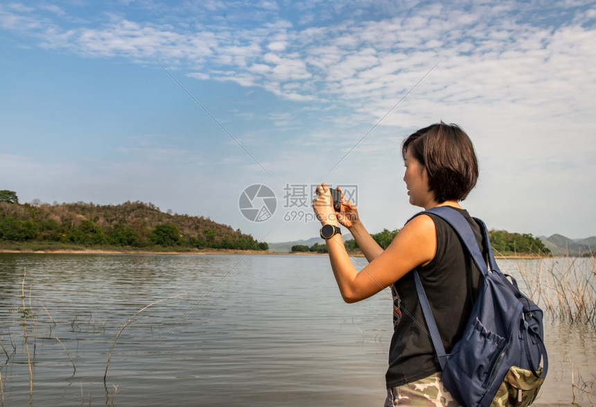 山一位年轻女使用智能手机的侧面观点并用它来拍摄湖边海岸的照片其背景包括技术节假日旅行生活方式自然没有重点具体来说就是无足轻重美丽图片