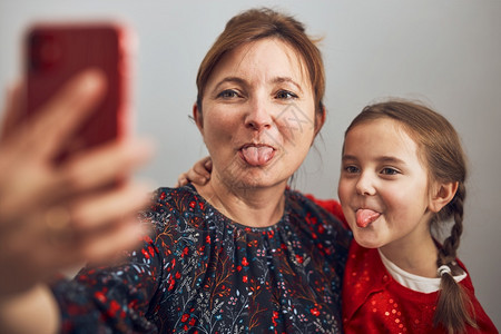 联系服用母亲和女儿手机打视频电话保持距离与家人的亲友聊天玩着自拍照使用智能手机与家人远程连线时家庭乐得开心人愉快在聊天中分享自拍图片