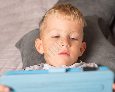 技术保持白种小男孩在家里躺床上时使用数字片子松弛图片