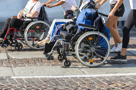 跑步者马拉松运动轮椅残疾员在马拉松运动车手帮助下女跑者残疾人运动员在马拉松轮椅上获得女跑者帮助经过身体的图片
