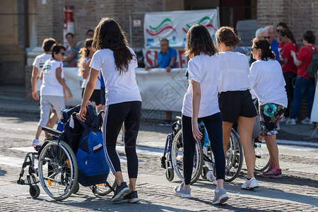 马拉松运动轮椅残疾员在马拉松运动车手帮助下女跑者残疾人运动员在马拉松轮椅上获得女跑者帮助决心移动支持图片