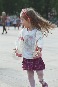 在镇中心玩肥皂泡的小快乐女孩儿童跑来去捕捉肥皂泡Candid人真实的瞬间现情况真正的天美丽图片