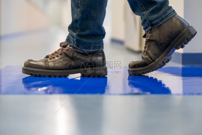 穿棕色鞋的男人踩着蓝色粘黏胶板控制塑料地面图片