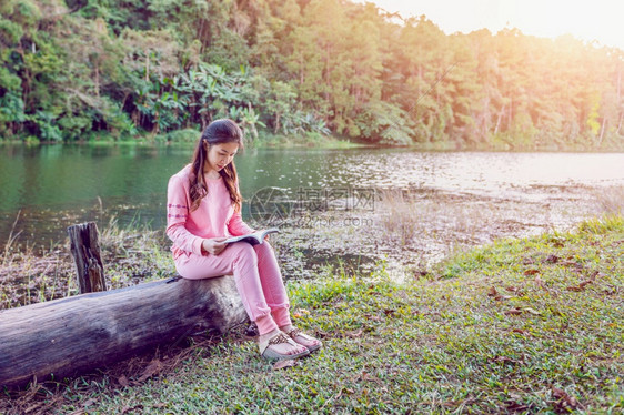 春天在河边坐在树干上读书的女孩图片