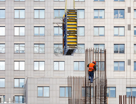 新的户外身穿明橙色背心的建筑工和高处安全头盔在新房子窗外的背景下用钢加固铁制成的金属板体结构图案身戴亮橙色背心的建筑工和安全头盔图片