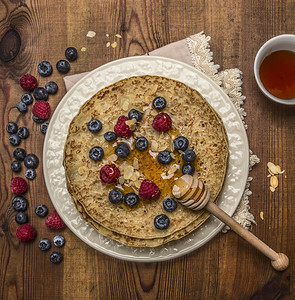 甜的早餐热美煎饼在白盘上餐巾纸配有蜂蜜和汤匙杏仁蓝莓和草还有一杯茶在生皮木本底顶端图片