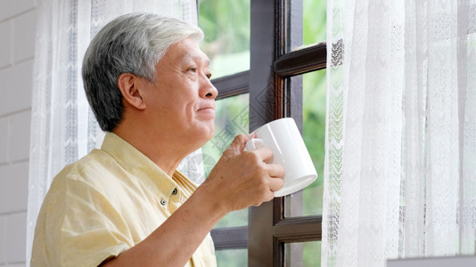 肖像饮料脸老年人在早上站窗前喝咖啡时快乐的年长老人在家里拿着咖啡杯退休老人健康生活方式AHLE图片