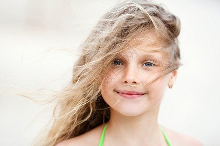 可爱的近距离接一个微笑的漂亮小女孩肖像坐在沙滩上风中挥舞长发美丽积极的图片