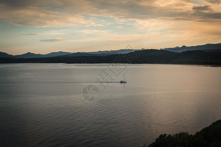 太平洋萨尔丁亚海岸与山丘和白帆船的萨丁尼亚海岸线意大利日落景观自然图片