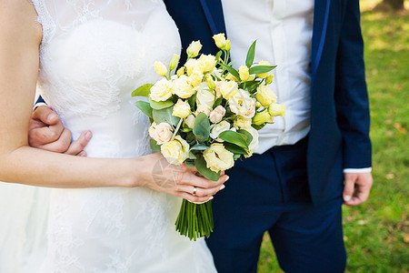 草地上的新婚夫妻手拿花束特写图片