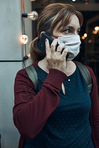 保持预防青年妇女通过电话交谈站在市中心餐馆门口的一家前面戴着罩以避免感染防止疾在出现冠状腺毒时传播b使用口罩避免感染防止疾蔓延保图片