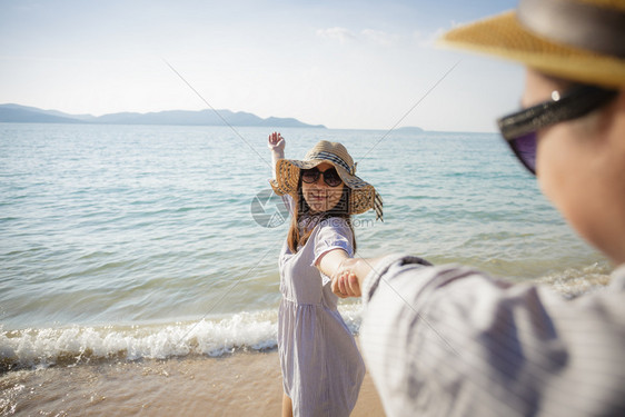 亚洲情侣在海滩上享受度假笑的女友带着她男朋的手走在海滩上相聚一番快乐的男人苏美尔图片