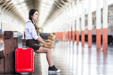 亚洲怀孕妇旅行者坐在火车站旅行时用红色手提箱拥抱TeddyBearTeddyBear夏天带背包的旅行者泰国度假概念旅游肖像亚洲人图片