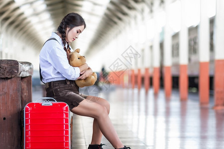 白色的红亚洲怀孕妇旅行者坐在火车站旅行时用红色手提箱拥抱TeddyBearTeddyBear夏天带背包的旅行者泰国度假概念旅游图片