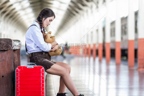 白色的红亚洲怀孕妇旅行者坐在火车站旅行时用红色手提箱拥抱TeddyBearTeddyBear夏天带背包的旅行者泰国度假概念旅游图片