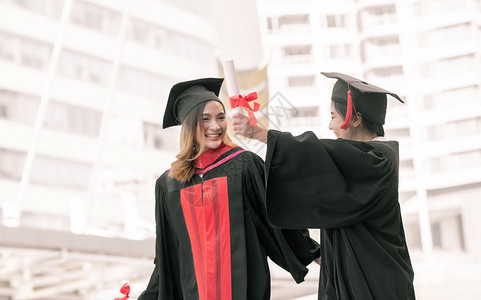 两位身穿红色学士服拿着毕业证书拍照的女学生仪式高清图片素材