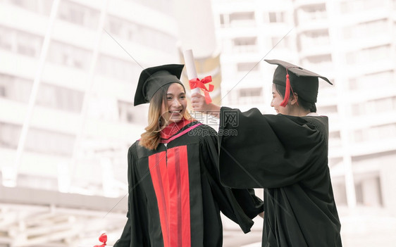 两位身穿红色学士服拿着毕业证书拍照的女学生图片