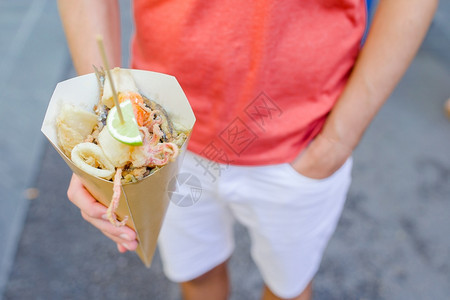 吃煮熟的纸意大利街头食品烤海鲜鱼虾鱿和蔬菜在男手中意大利街头食品烤海鲜鱼鱿和蔬菜图片