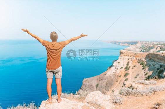 在悬崖边缘的快乐户外男人享受在山顶岩石上风景的欢快旅游者男子在悬崖海岸边缘风景请享用天快乐的图片