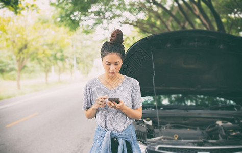 分解强调亚裔女在寻找时使用手机在街上因汽车故障而坐后修理图片