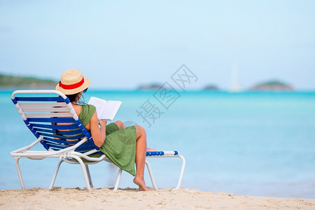 椅子气候享受年轻女在海滩上阅读关于沙的chaiiselounge的书图片