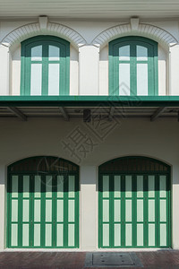 绿色木制折叠拱门的阳光和阴影窗户斜体套在垂直架子上的旧白色建筑墙上外部砖折叠式的图片