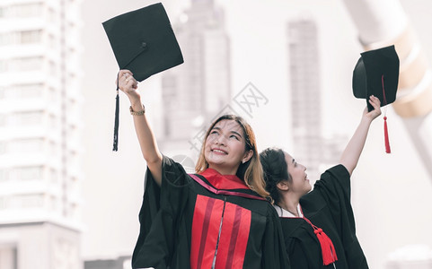 学校两名身着制服帽子和毕业后快乐笑的亚裔女学生教育概念户外年轻的团队合作高清图片素材