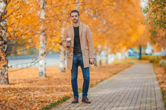 一次穿着棕色大衣男人在秋天公园喝咖啡在秋天公园户外喝咖啡的年轻男子生森林图片