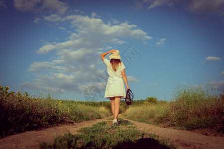 离开夏日穿着白衣服戴帽子站在泥土路上的白衣年轻女子肖像走出后视线户外真实的图片