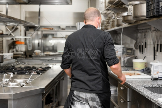 信心在一家商业厨房做饭时身着围裙的男厨员在房柜台旁站立准备食物一名商业厨房做工时身着制服烹饪衣物的优质摄影师在做饭时身着围裙的男图片