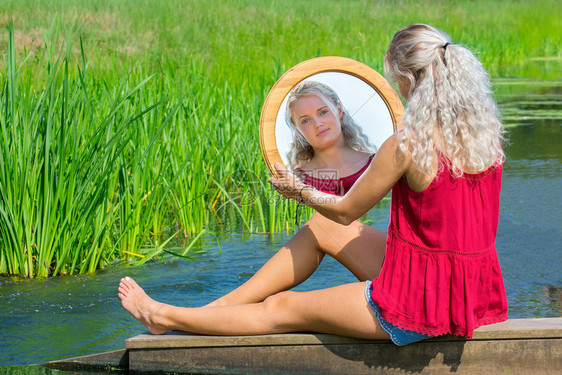 年轻的欧洲金发女郎坐在水面照镜子脸公园闲暇图片