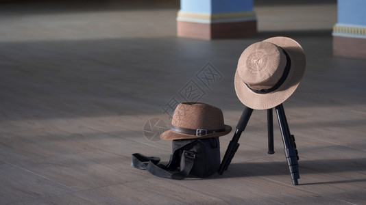 内部的淑女个人士帽和Fedora帽子表面的阳光和阴影挂在照相机三脚架上用黑色摄像袋挂在木砖地板上以古老的音调风格爱情和旅行概念中图片