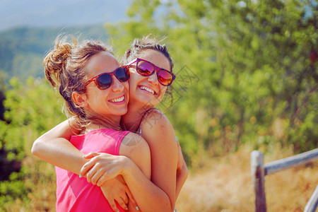 乐趣有两个美丽的年轻女孩朋友或姐妹在大自然中玩得开心在秋天旅行时拥抱着彼此微笑地拥抱对方穿着夏装太阳墨镜农村白种人图片