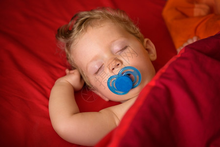睡眠八个月大的婴儿男孩在红背景的嘴里睡着与大豆同就寝时间纯真图片