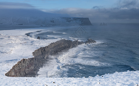 自然旅行天冰岛Dyrholaey角海岸景观的全图象在冬季与积雪覆盖海岸线的冰岛图片