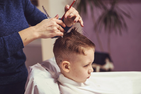 男时髦肖像理发师孩子的小男害怕剪发师对小男孩的手做发型关上男孩时装发型的图片